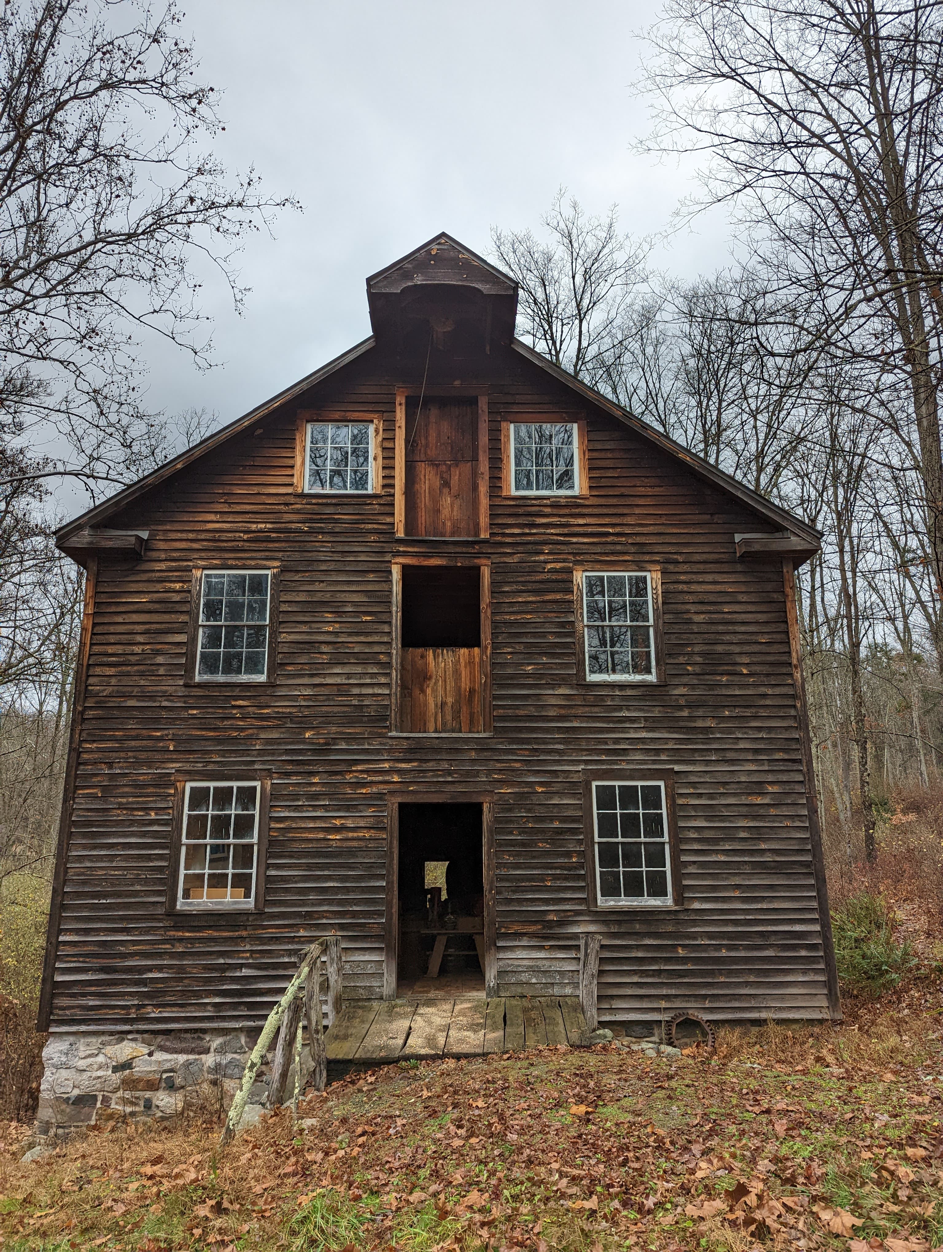 A wooden grist mill three stories tall surrounded by fallen leaves.