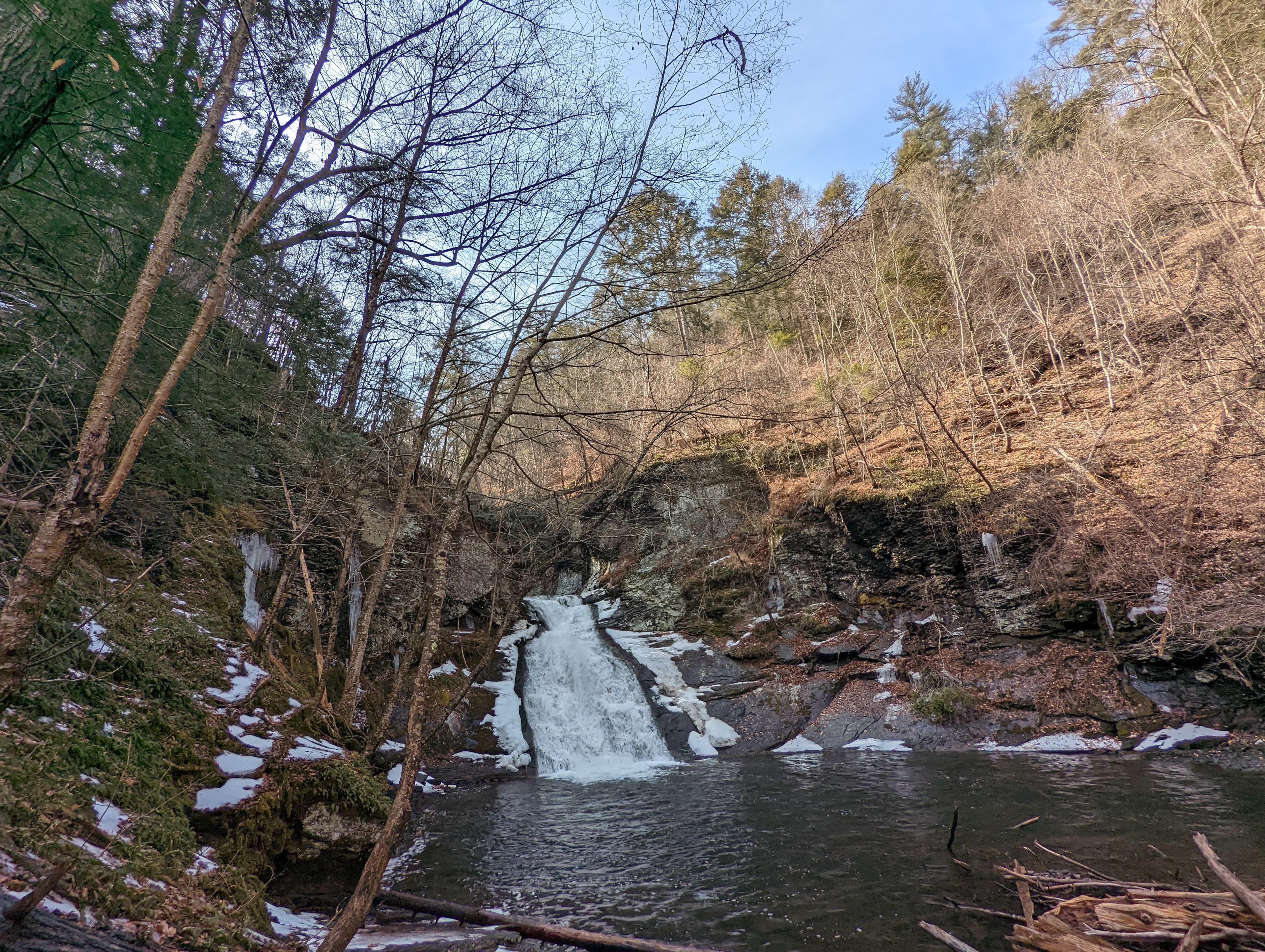 A small, tiered waterfall and pool with a small amount of snow around it.