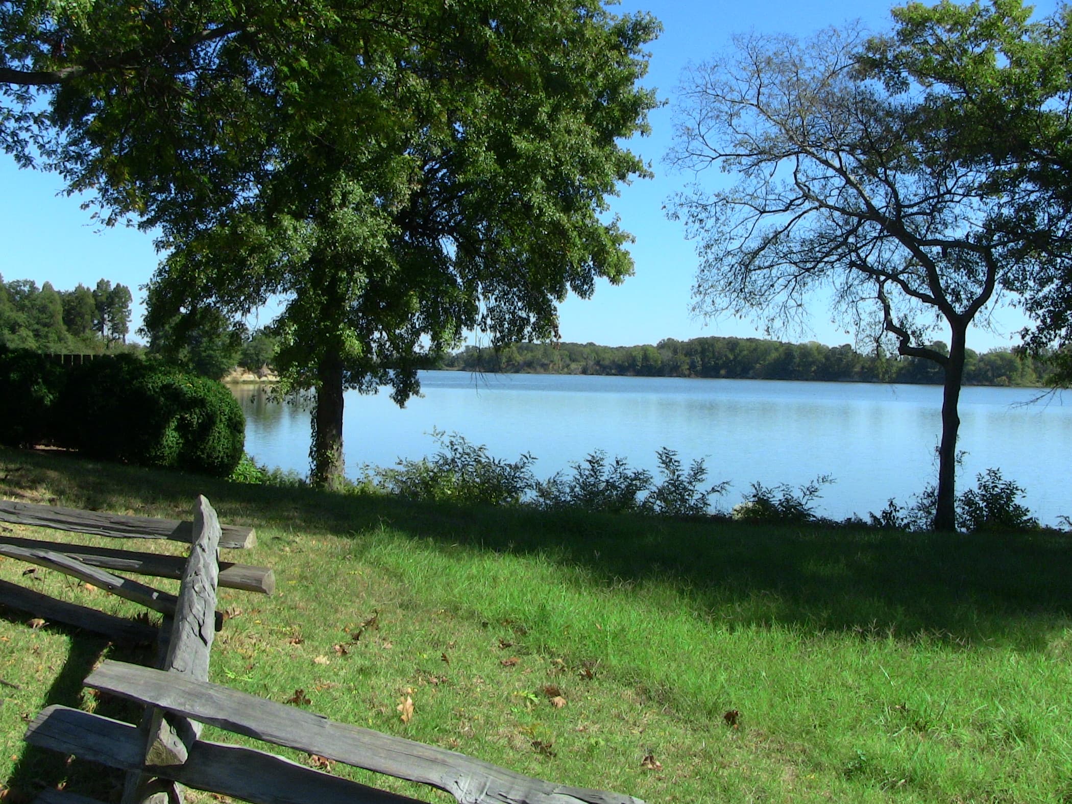 view of wide, tidal creek with trees and split rail fence in foreground