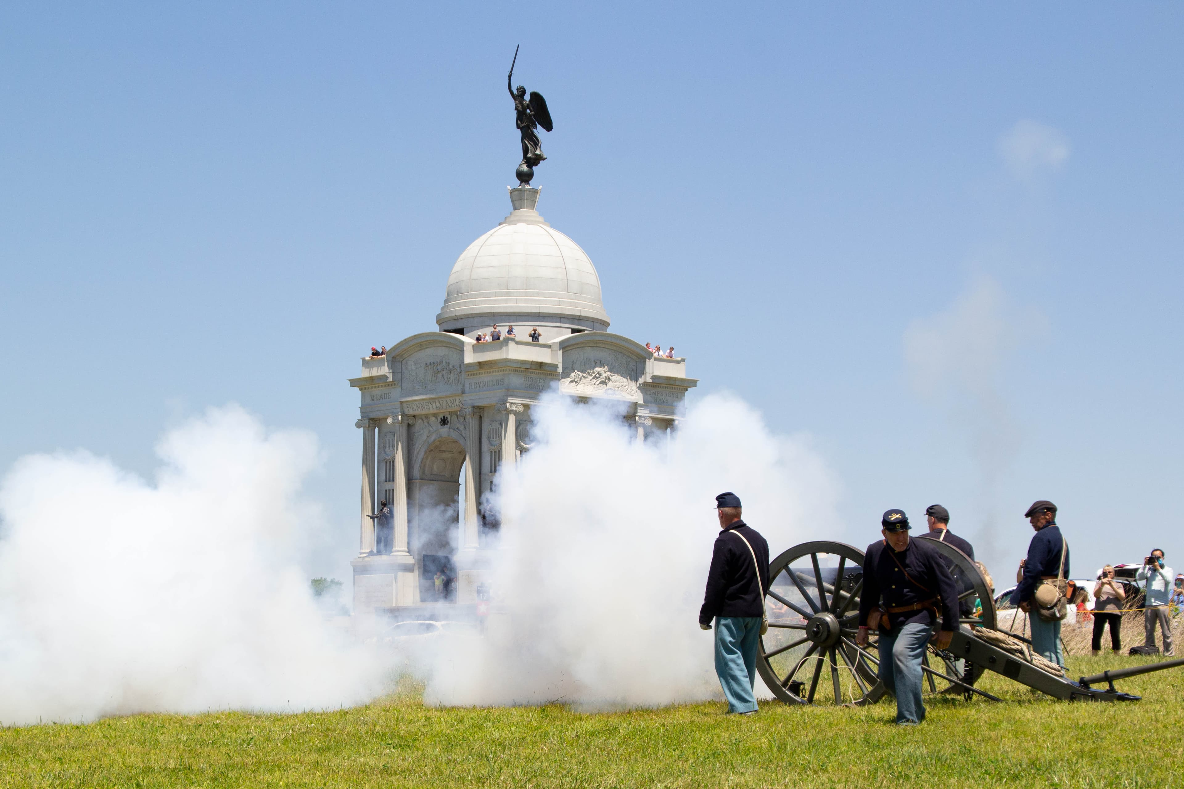 Living history volunteers fire a civil war cannon in front of a white, domed monument.