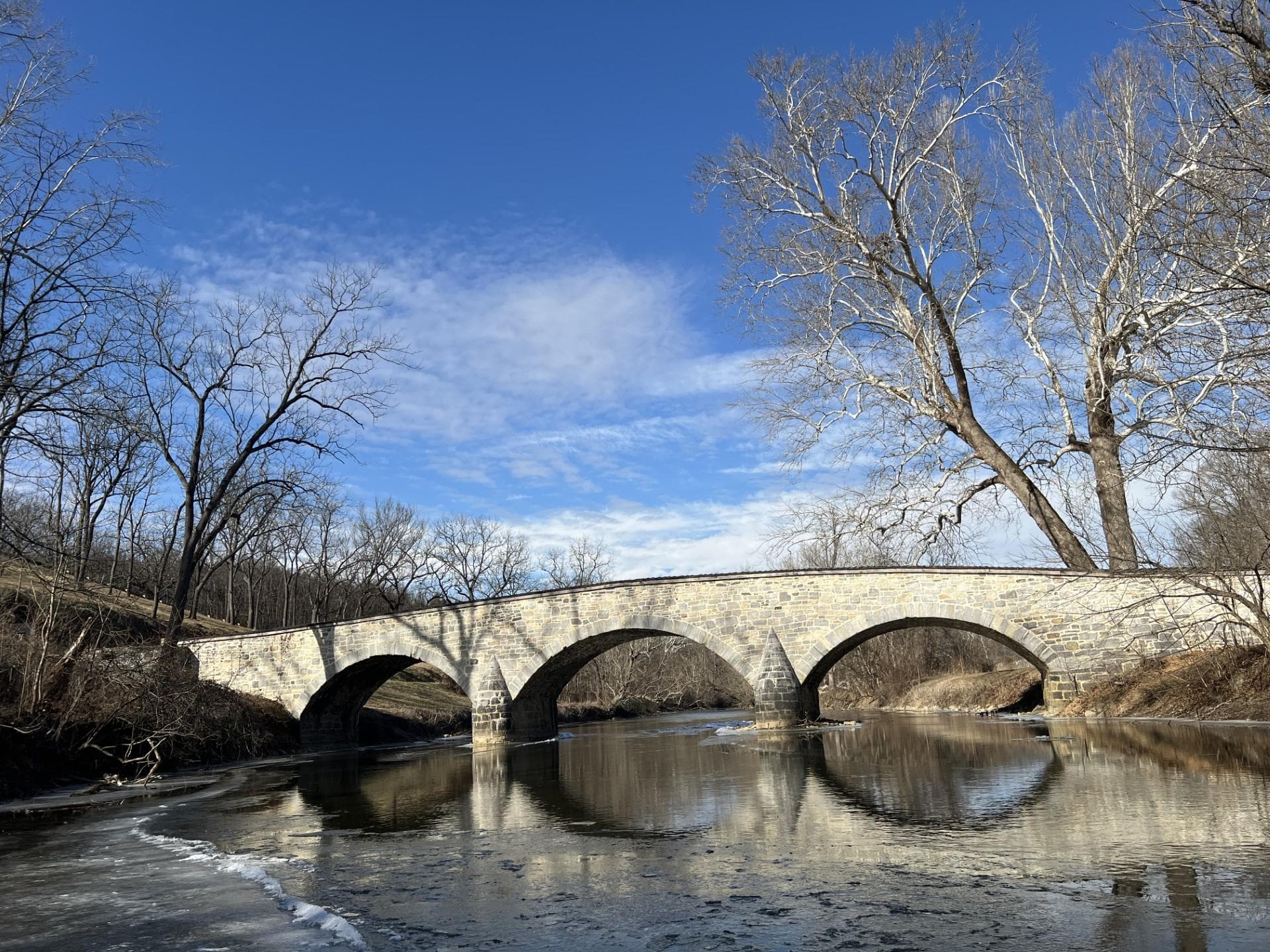 Antietam Creek flows under a three arch stone bridge blue sky